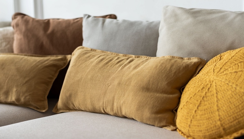 A cozy arrangement of various textured pillows in earthy tones, including mustard yellow and brown, on a neutral-colored sofa, creating a warm, inviting atmosphere.