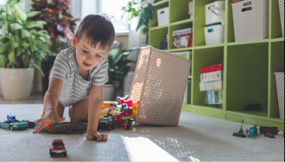 A cheerful European boy plays with colorful cars on the carpet in his room. 