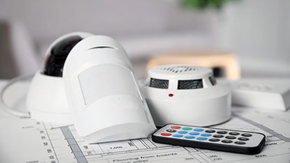 CCTV camera, remote control, smoke and movement detectors on building plan indoors. Home security system 