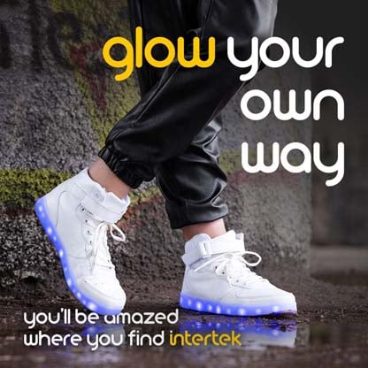 A closeup of a pair of white sneakers with lights along the soles being worn in the rain